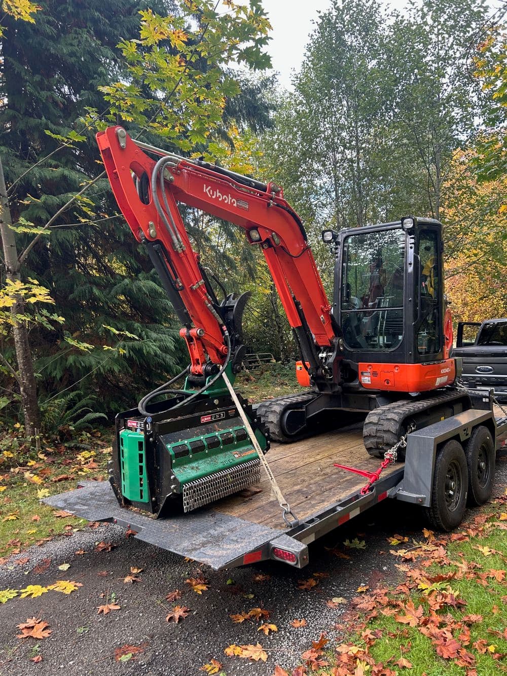 Kubota excavator on trailer surrounded by autumn foliage, ready for landscaping work.