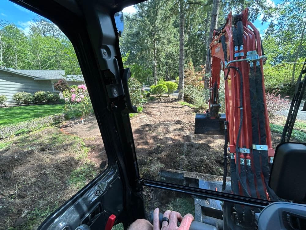 Excavator operator's view while landscaping a garden with freshly disturbed soil.